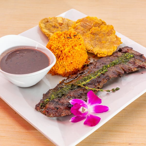 Cuban skirt steak with green sauce, yellow rice, fried plantains, black beans, and an orchid.