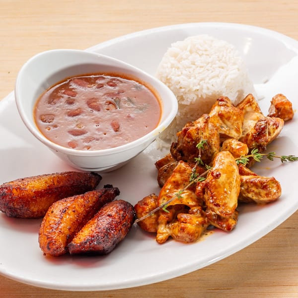 Cuban meal with chicken, rice, red beans, and fried plantains on a white plate.