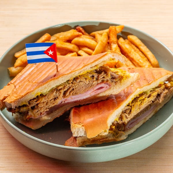Cuban sandwich with a Cuban flag pick and a side of golden french fries on a teal plate.