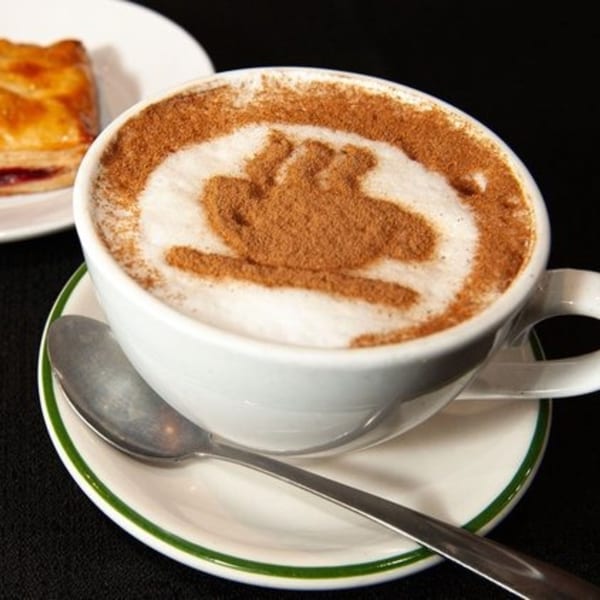 Cuban coffee with cinnamon art on top, served with a pastry on a white plate.