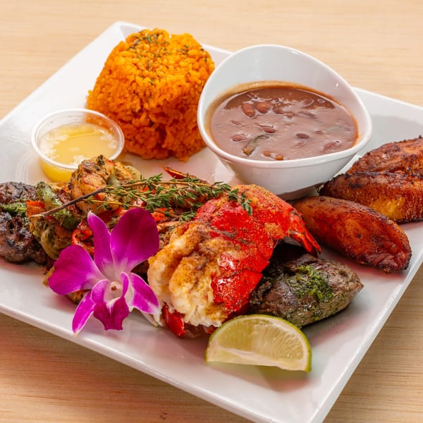 Cuban surf and turf with lobster, steak, shrimp, rice, beans, plantains, and a purple orchid.