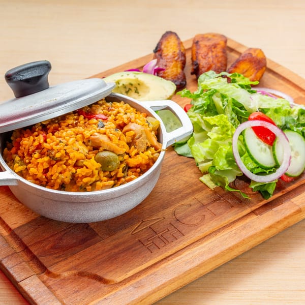 Cuban chicken and rice in a pot, with fried plantains, avocado, and a fresh salad.