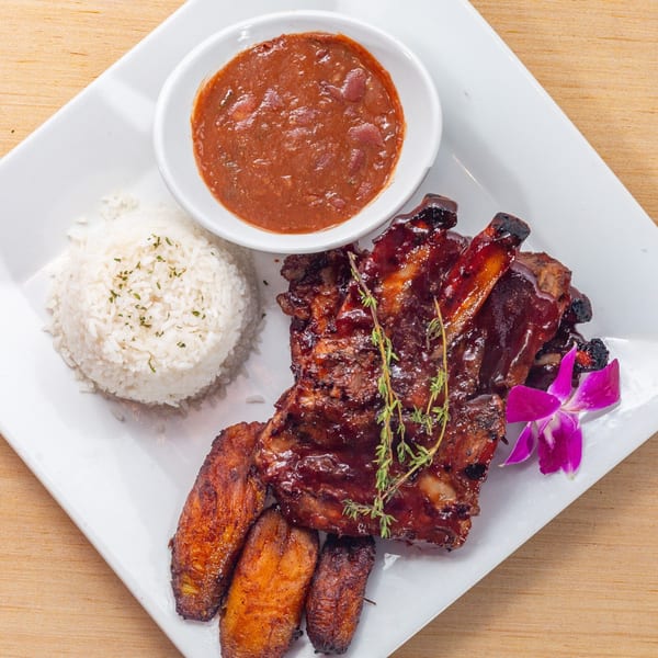 Cuban BBQ ribs with rice, red beans, fried plantains, and an orchid garnish on a white plate.