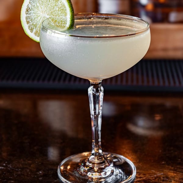 A frosty Cuban daiquiri cocktail with a lime slice garnish, on a dark bar top.