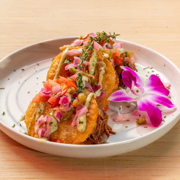Cuban tostones topped with shredded meat, salsa, green sauce, and a purple orchid garnish.