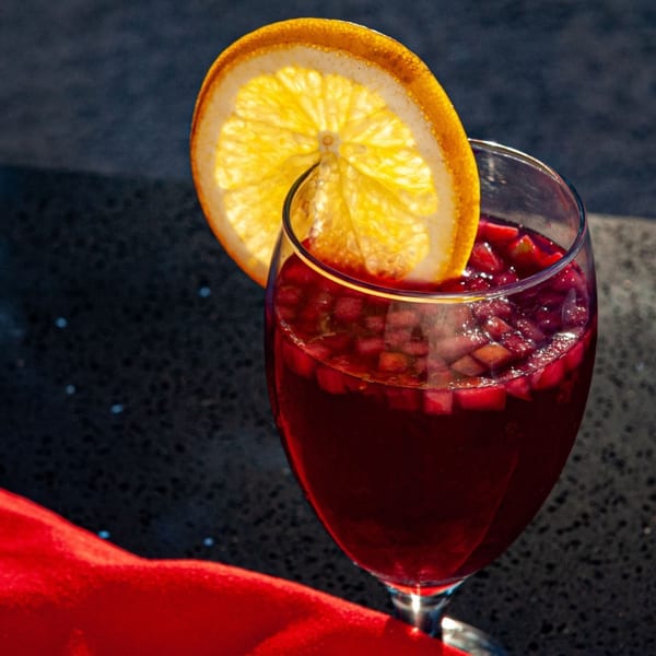 Close-up of a glass of red sangria with diced fruit and an orange slice garnish.