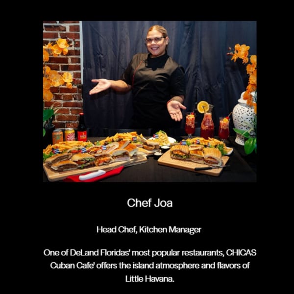 Chef Joa smiling behind a table laden with Cuban sandwiches, fries, and drinks at Chica's Cuban Cafe.