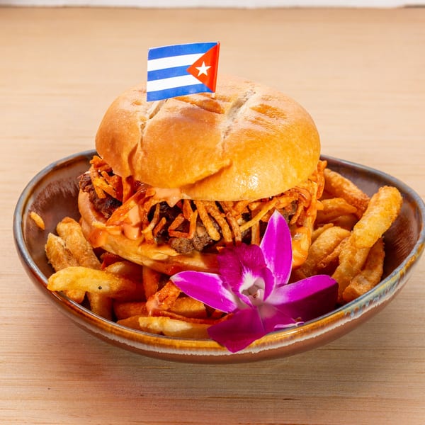 Cuban burger with crispy shoestring potatoes and a Cuban flag pick, served with fries and an orchid.