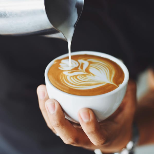 A barista pours milk into a white cup of coffee, creating latte art at Chica's Cuban Cafe.